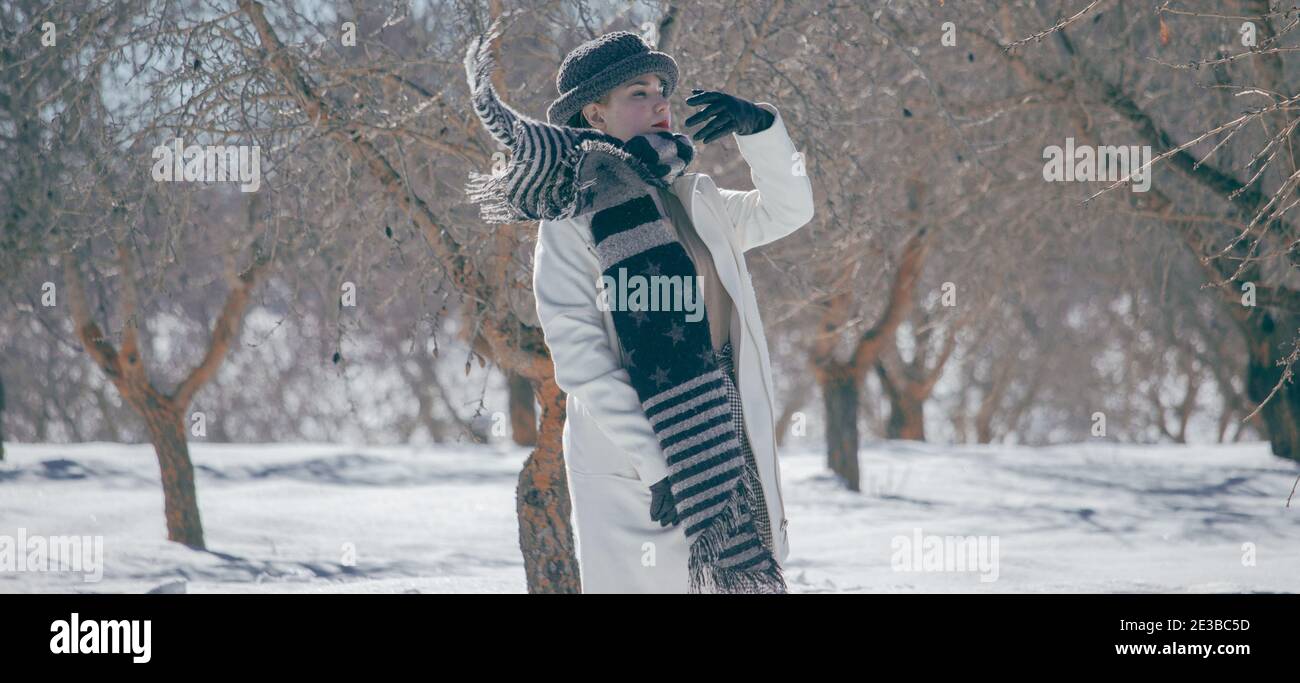Schöne junge Frau setzt ihren schwarzen Schal in einem kalten Tag von verschneiten Natur umgeben. Winter Wald Landschaft Hintergrund. Snow Concept 2021. Stockfoto
