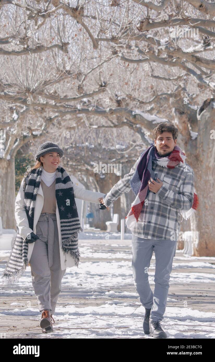 Junges Paar haben Spaß, die Hände in einem verschneiten Tag halten, während beide glücklich zu Fuß sind. Winter Im Freien 2021. Stockfoto