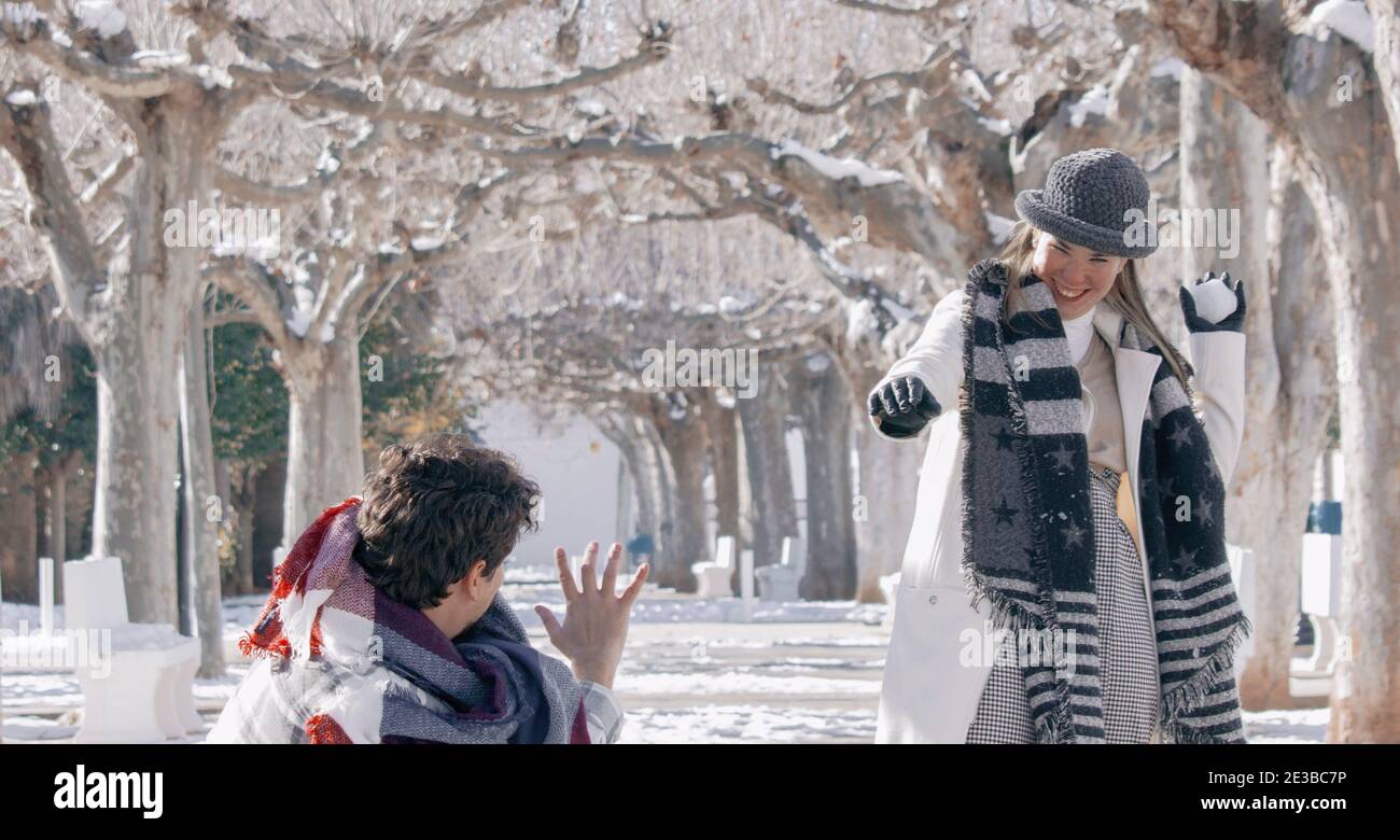 Junges Paar spielt auf dem Schnee an einem Wintertag im Freien. Freundin wirft Freund einen Schneeball lächelnd auf ihn. Winterfotografie 2021. Stockfoto