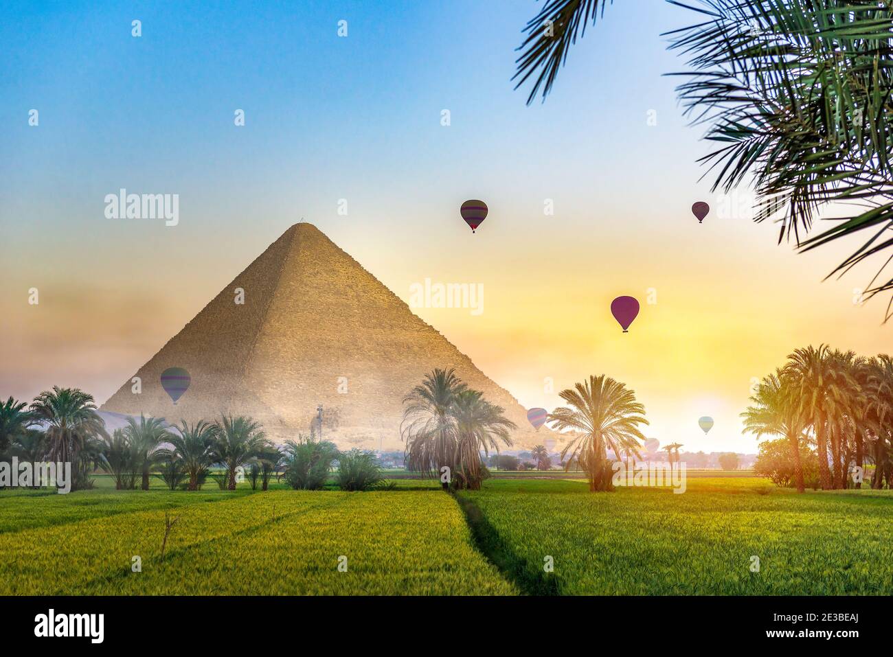 Luftballons über der ägyptischen Pyramide im grünen Feld am nebligen Morgen. Fantasielandschaft mit ägyptischer Pyramide Stockfoto