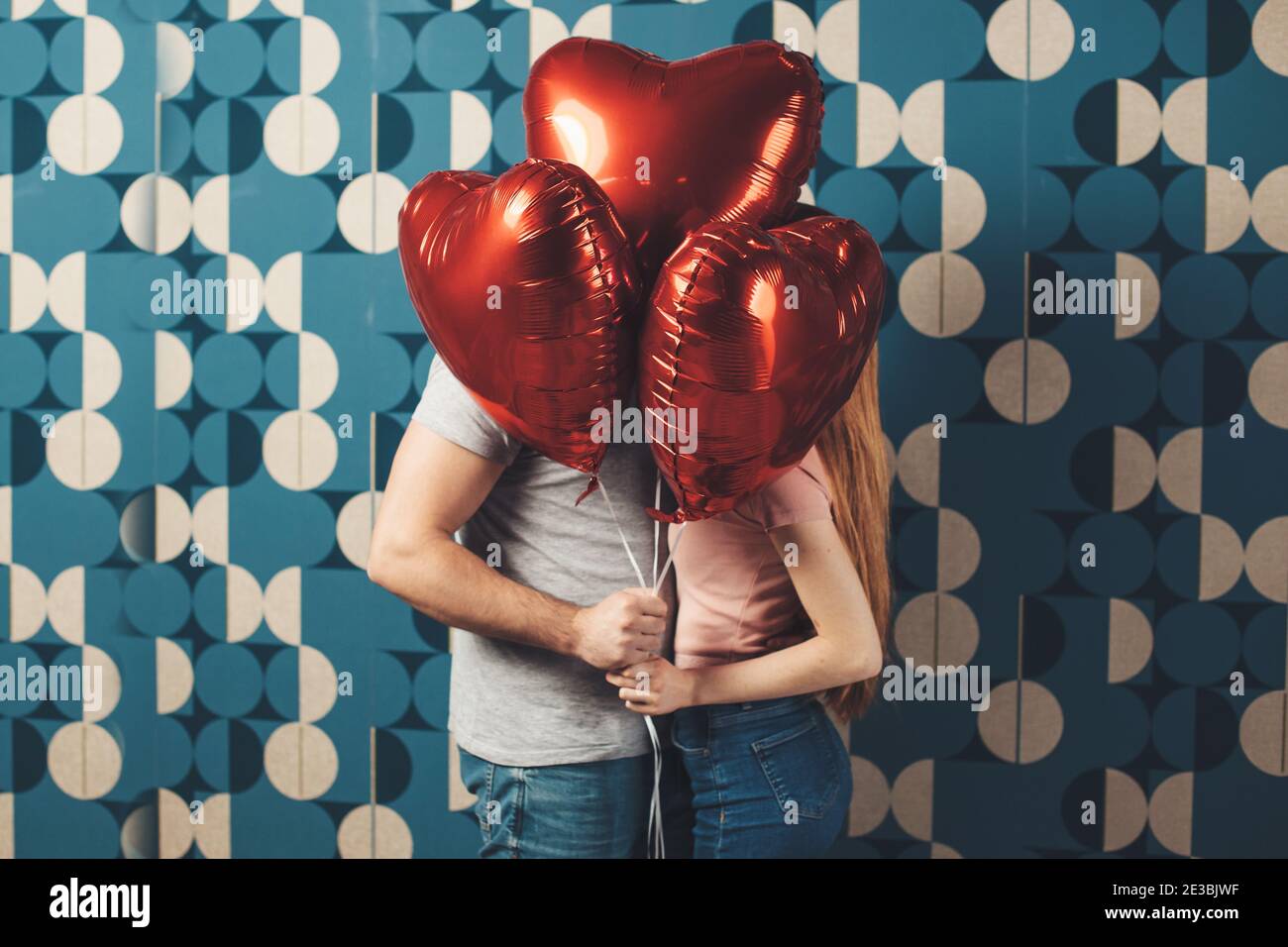 Kaukasisches Paar küsst sich hinter den Ballons an einer blauen Wand Wir feiern den Valentinstag Stockfoto