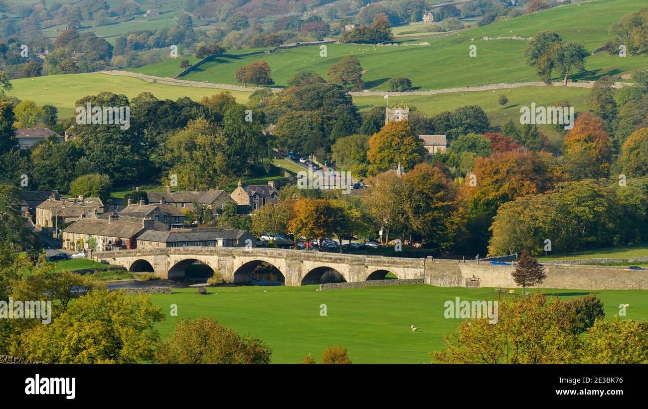 Malerische sonnige Burnsall Dorf (5-gewölbte Steinbrücke, Fluss Wharfe, Hütten, Kirche, Hügel Felder, Herbstbäume) - Yorkshire Dales, England. Stockfoto