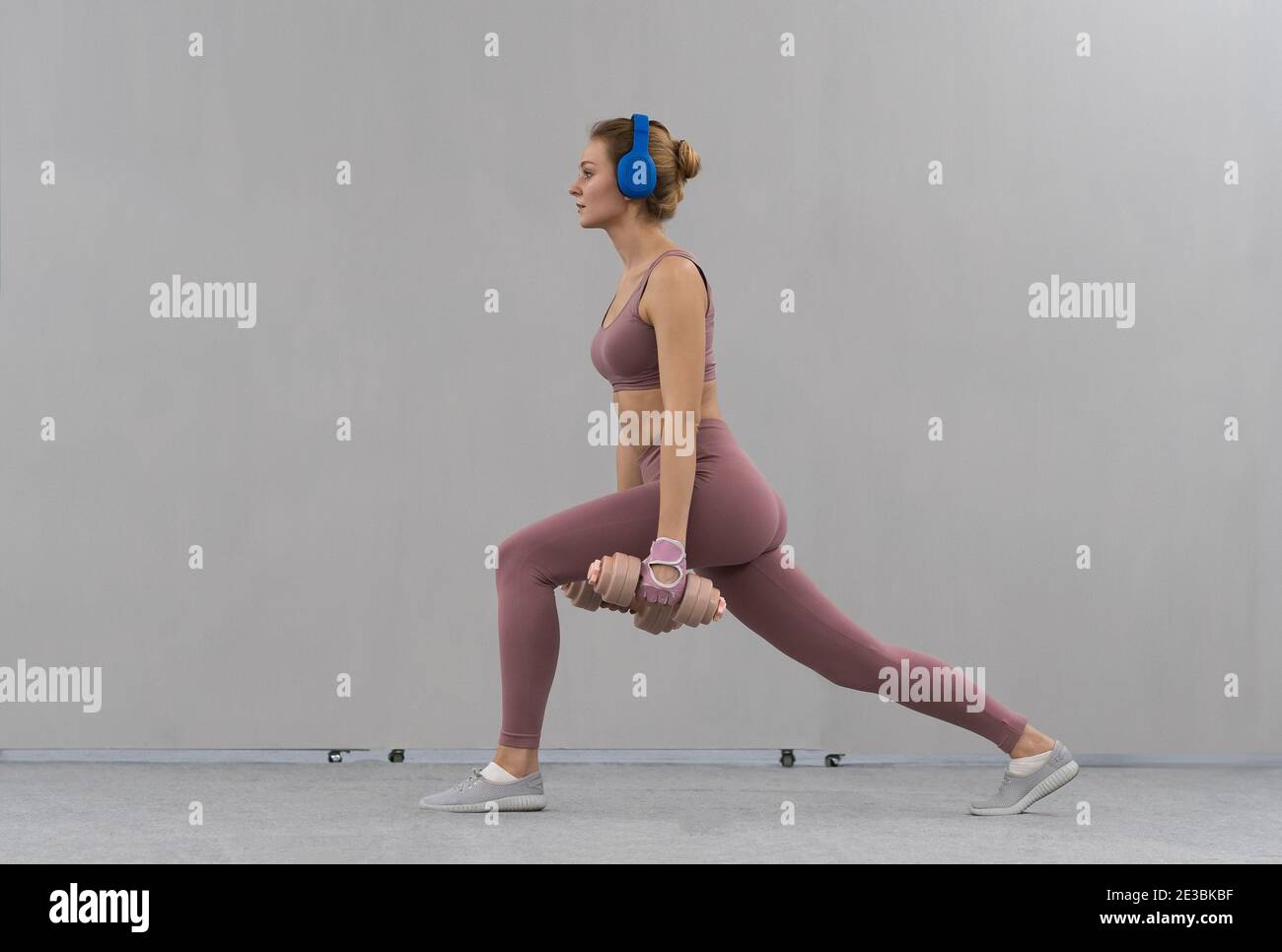 Stretching mit Hanteln mit Händen nach unten junge Mädchen Gewicht zu Hause tragen rosa Outfit verlieren, während Musik in blauen kabellosen Kopfhörern hören. Sport Stockfoto