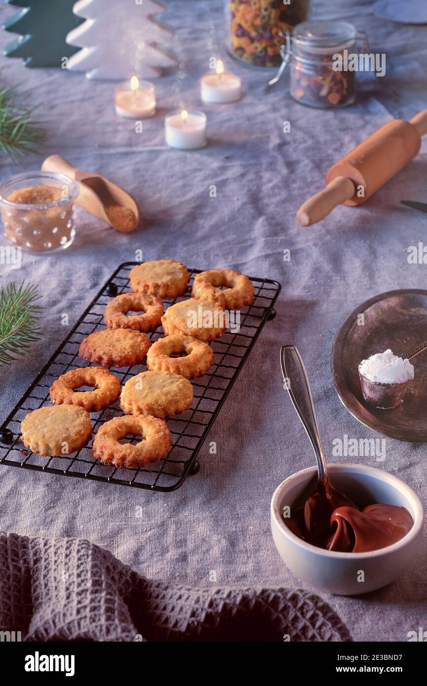 Sandwichkekse gefüllt mit Haselnussaufstrich, Nougatcreme. Weihnachtsbäume, Kerzen auf Leinentischdecke. Tageslicht. Stockfoto