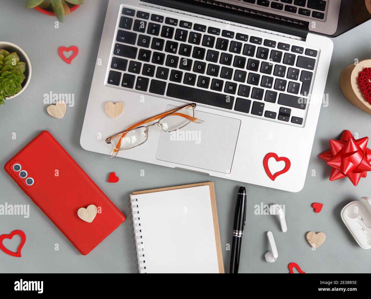 Rote Handy, Notebook, Brille und Valentinstag Dekoration in der Nähe Laptop Draufsicht auf grauen Tisch Stockfoto