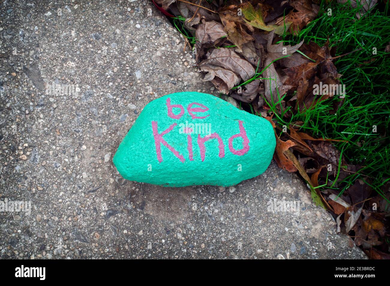 VOLKSKUNST. Ein hell bemalter Stein mit dem Vorschlag, freundlich zu sein. In einer Einfahrt in Flushing, Queens, New York City. Stockfoto