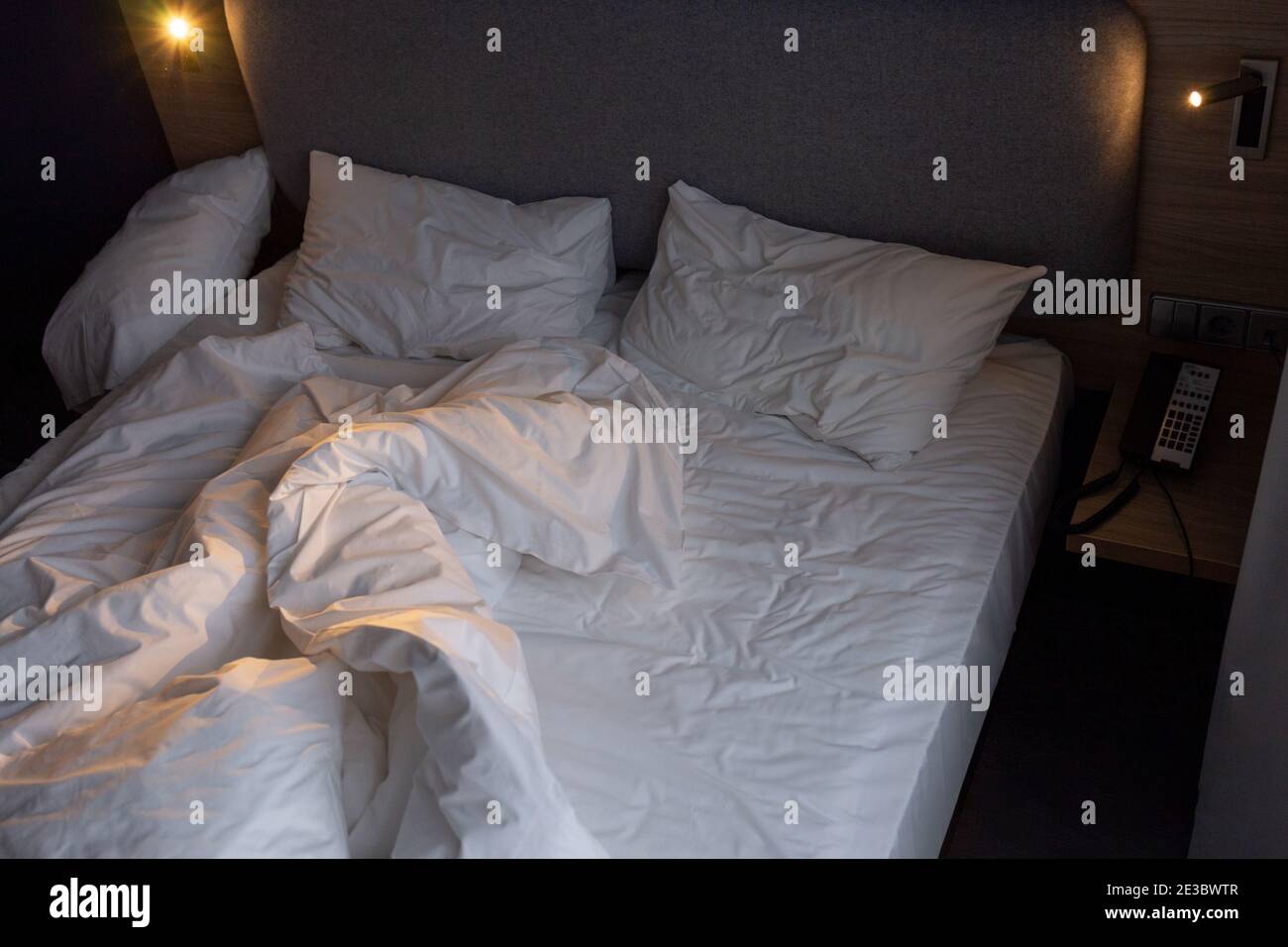 Ungemachtes leeres Bett in einem Hotelzimmer. Schwaches Licht Stockfoto