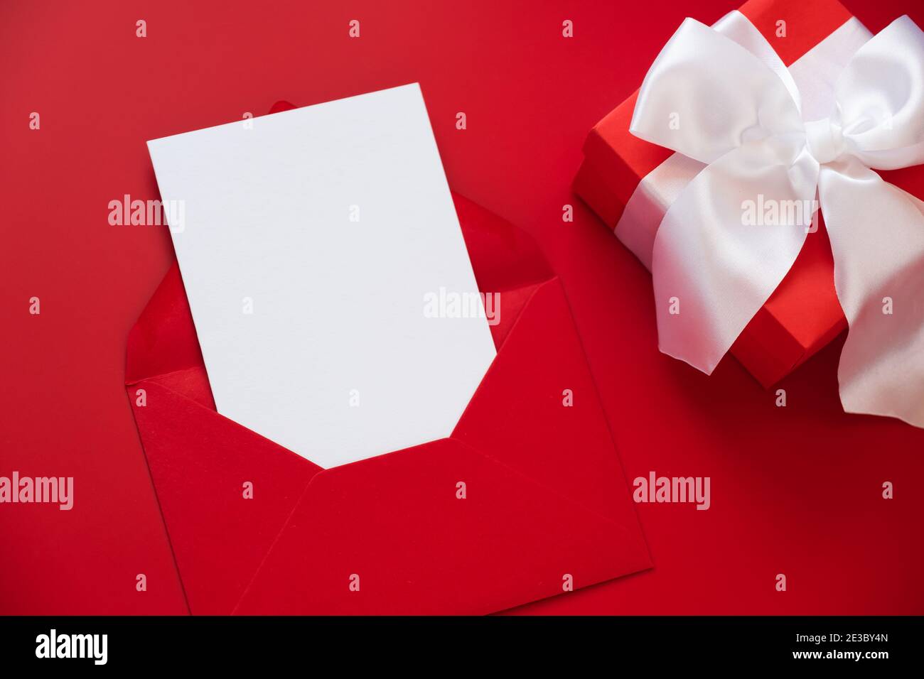 Grußkarte Mockup, weiße leere Karte im Umschlag und Geschenkbox auf rotem Hintergrund. Alles Liebe zum Valentinstag oder zum Muttertag. Flach liegend, Draufsicht. Stockfoto