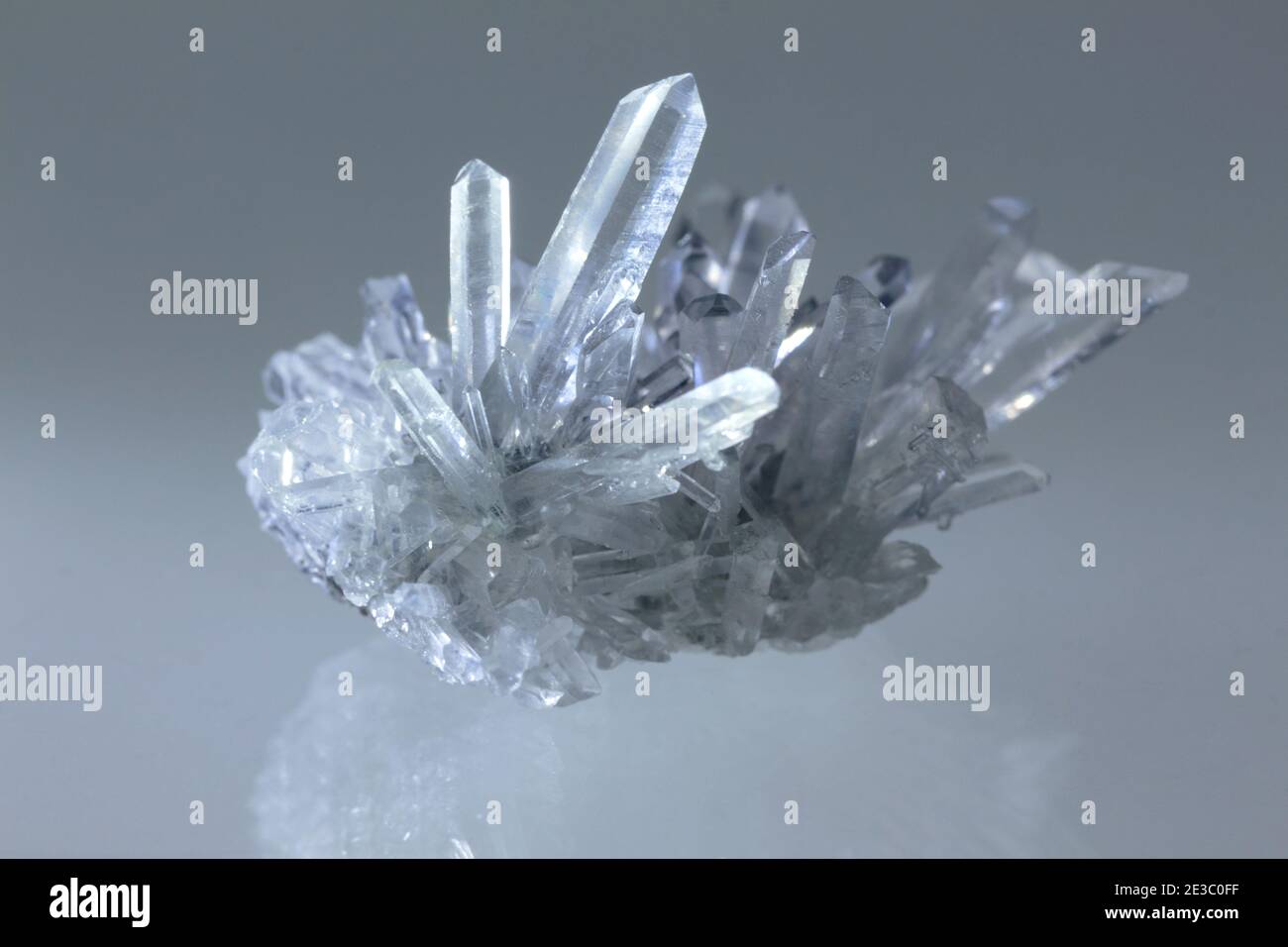 Ein rohes klares Quarzkristall-Cluster-Mineral-Exemplar auf einem Weißer reflektierender Hintergrund mit dramatischer Beleuchtung, die ihn schimmern lässt Und Leuchten Stockfoto