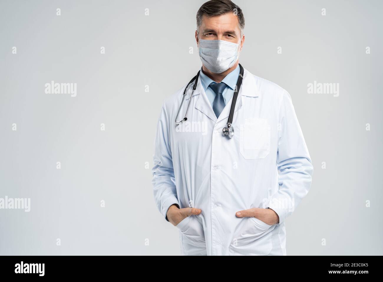 Heiter reifer Arzt in Gesichtsmaske posiert bei Kamera, Gesundheit und Medizin. Stockfoto