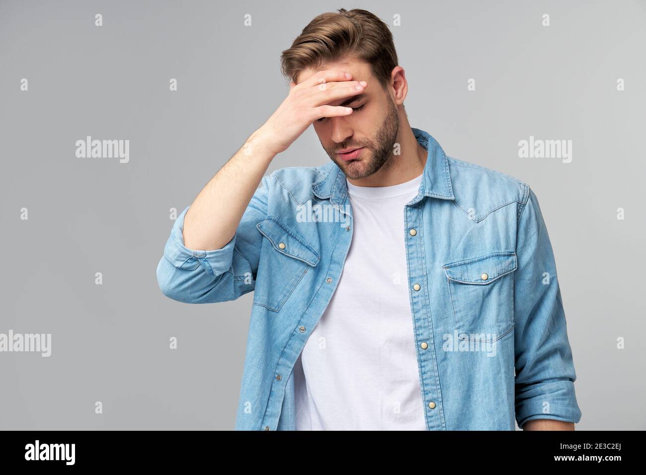 Frustriert junge kaukasischen Mann in Jeans Hemd berühren Kopf mit Hand im Stehen überg Studio grauen Hintergrund Stockfoto