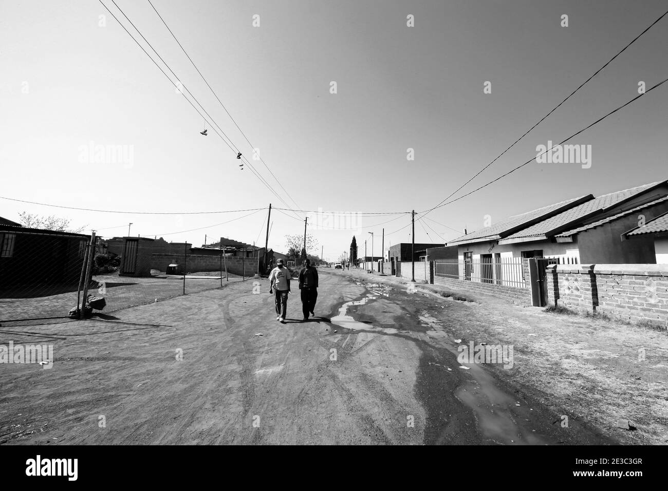 JOHANNESBURG, SÜDAFRIKA - 05. Jan 2021: Soweto, Südafrika - 10. September 2011: Zwei afrikanische Männer, die auf einer unbefestigten Straße in der Nachbarschaft im Sowet spazieren Stockfoto