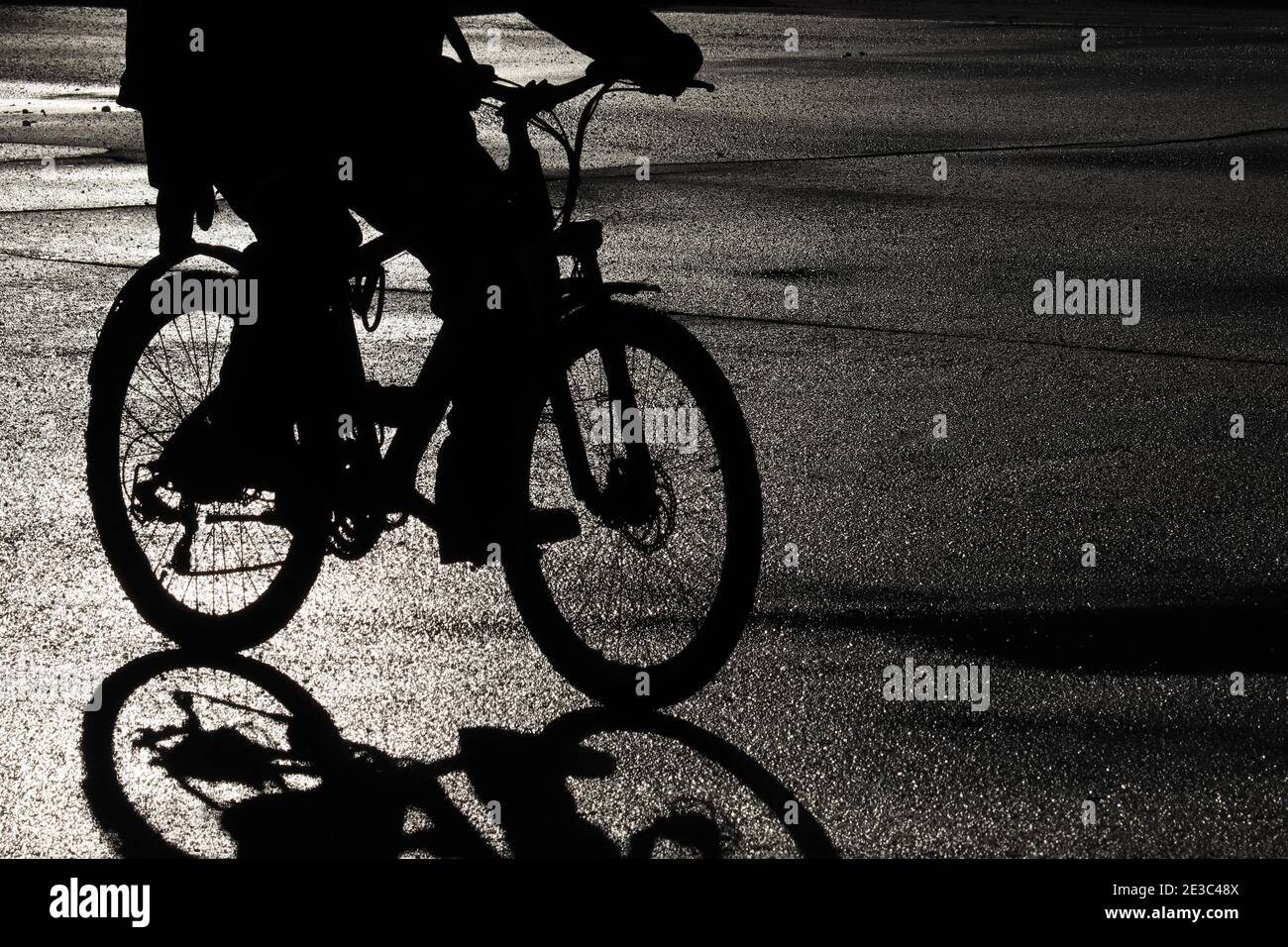 Schwarze Silhouette eines Radfahrers auf der nassen Straße. Person auf dem Fahrrad, Fahrrad-Konzept, dramatische Atmosphäre Stockfoto