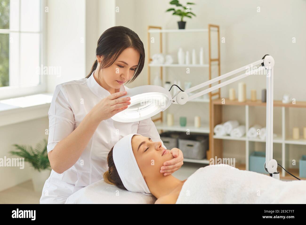 Dermatologe lenkt Lampe auf das Gesicht der Frau während der Überprüfung der Haut Stockfoto