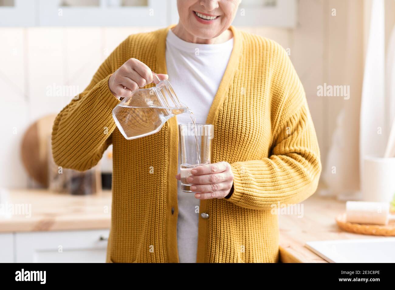Nahaufnahme einer nicht erkennbaren Großmutter, die Wasser in das Glas gießt Stockfoto