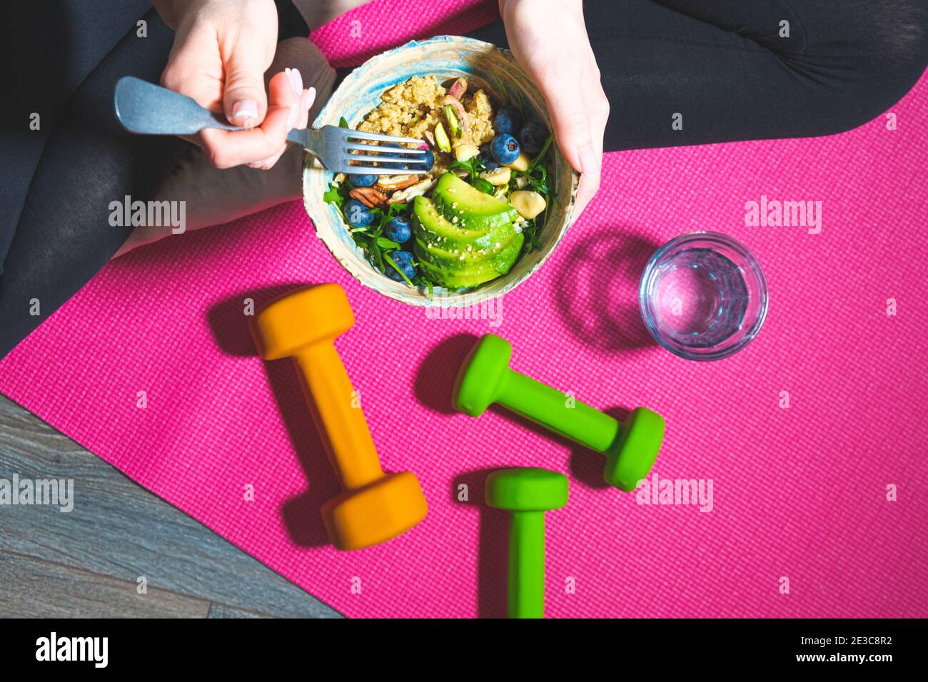 Frau auf der Fitnessmatte, die nach dem Training einen gesunden veganen Salat isst. Vegane Ernährung und Sportkonzept. Stockfoto