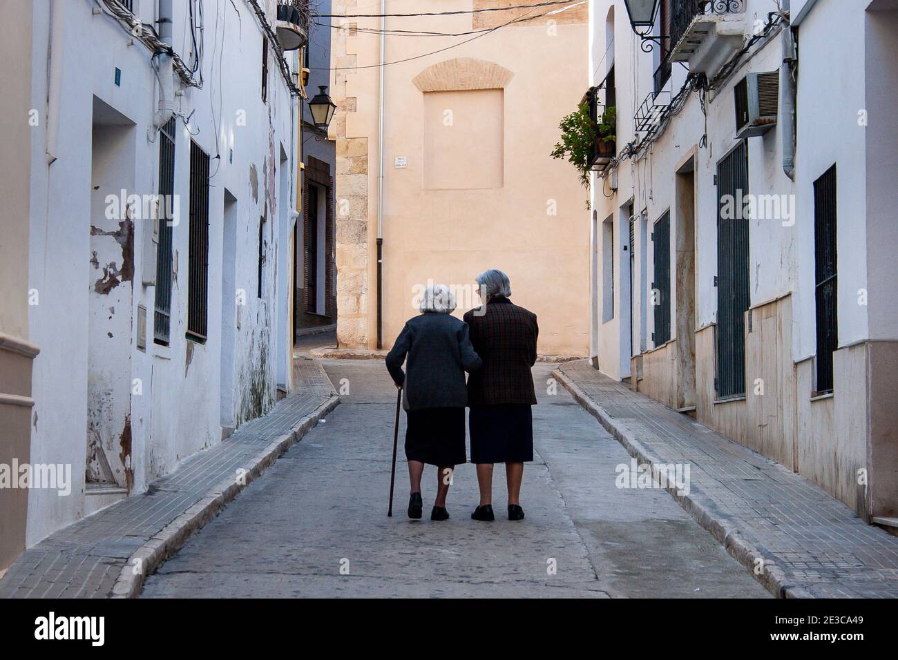 Zwei alte Damen gehen eine enge Straße hinauf, die Arme verbindet In der Altstadt von Oliva in der Region Valencia Spanien Stockfoto
