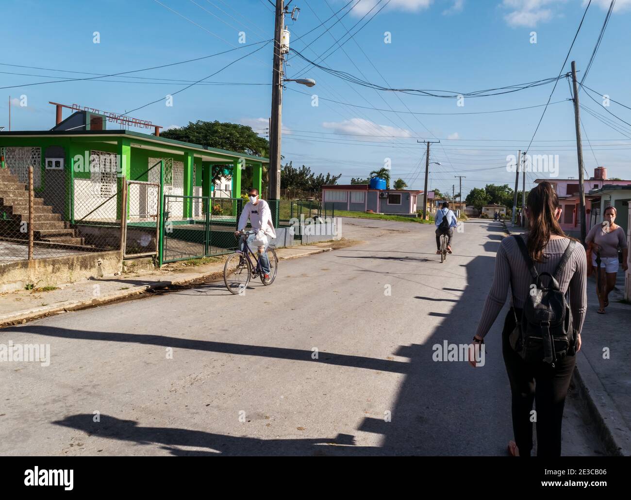 Foto einer Straße in einer kleinen Stadt in Kuba, in der während einer Pandemie nur wenige Menschen auf der Straße unterwegs sind, fahren zwei Männer mit dem Fahrrad und zwei Frauen laufen Stockfoto