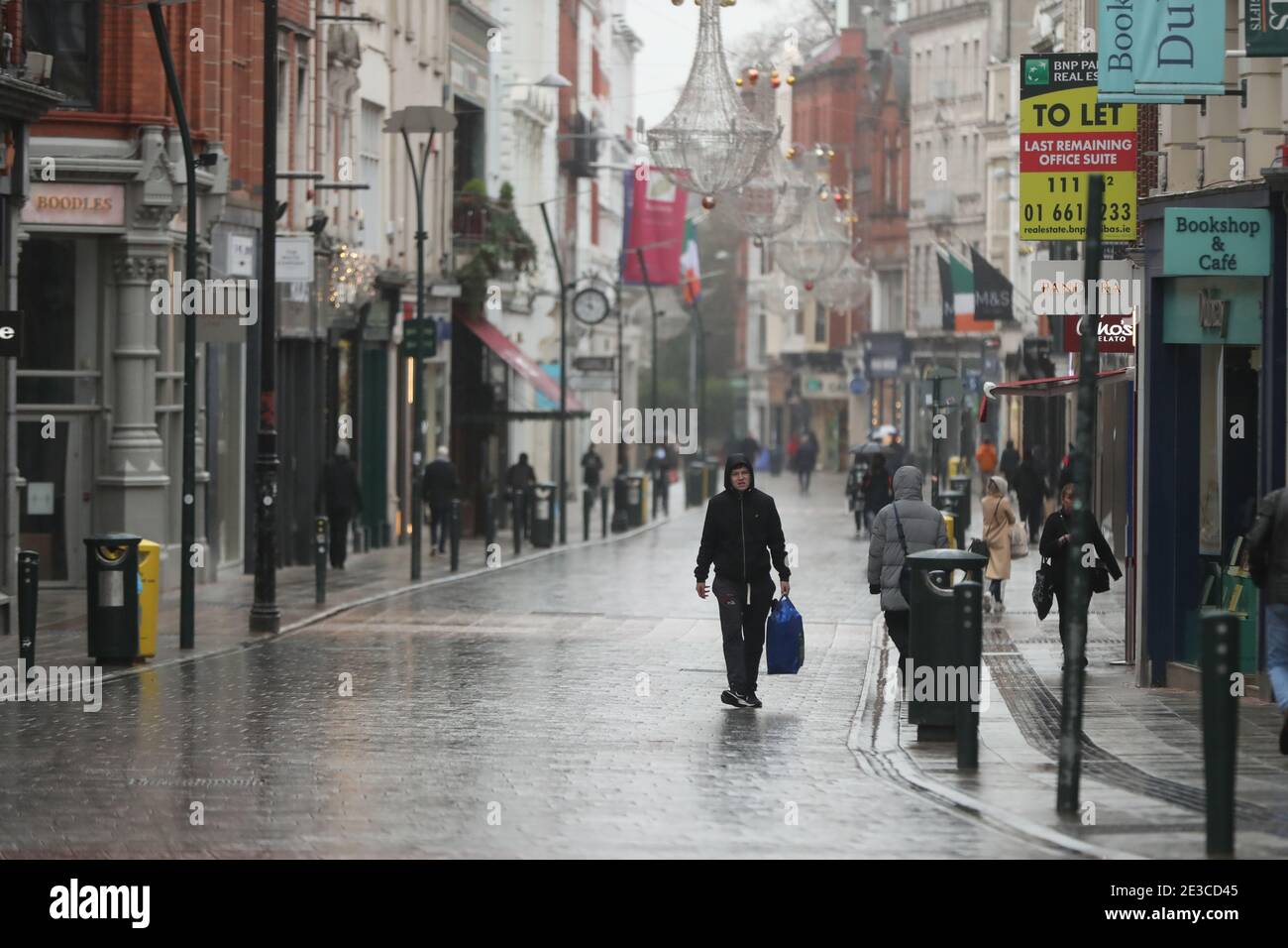Die Menschen laufen entlang einer nahe leeren Grafton Street im Stadtzentrum von Dublin, während Irland in der Sperre bleibt, um die Ausbreitung des Coronavirus zu verhindern. Irlands Gesundheitswesen steht möglicherweise vor der schwierigsten Woche seiner Geschichte: Die Zahl der Covid-19-Patienten, die eine Intensivbehandlung benötigen, ist seit Ende Dezember stark gestiegen. Bilddatum: Montag, 18. Januar 2021. Stockfoto