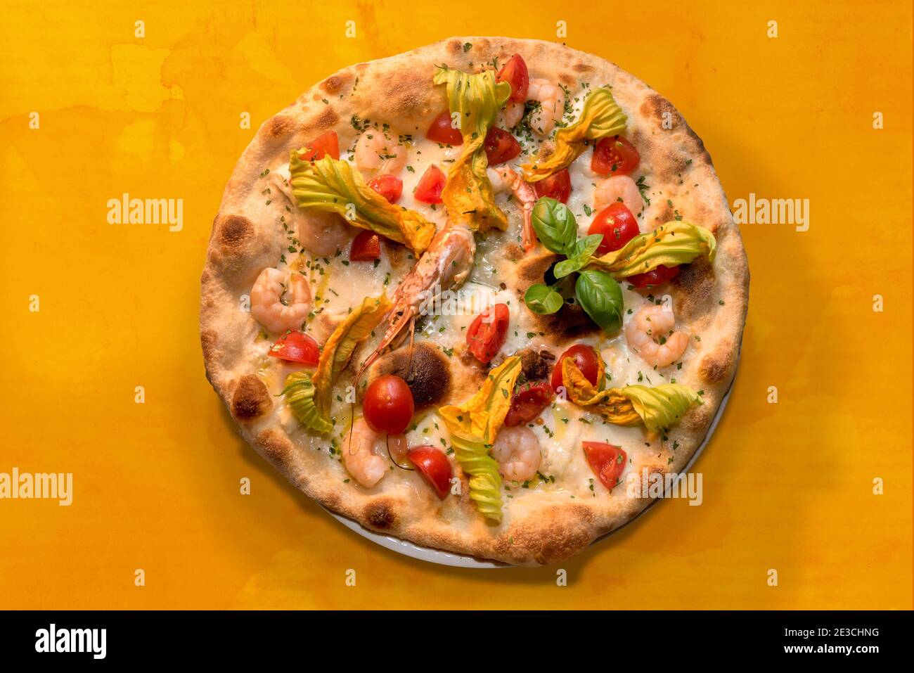 Pizza mit Garnelen, Zucchini-Blumen, Kirschtomaten und Mozzarella-Käse, Draufsicht flach auf orangefarbenem Aquarell-Hintergrund Stockfoto