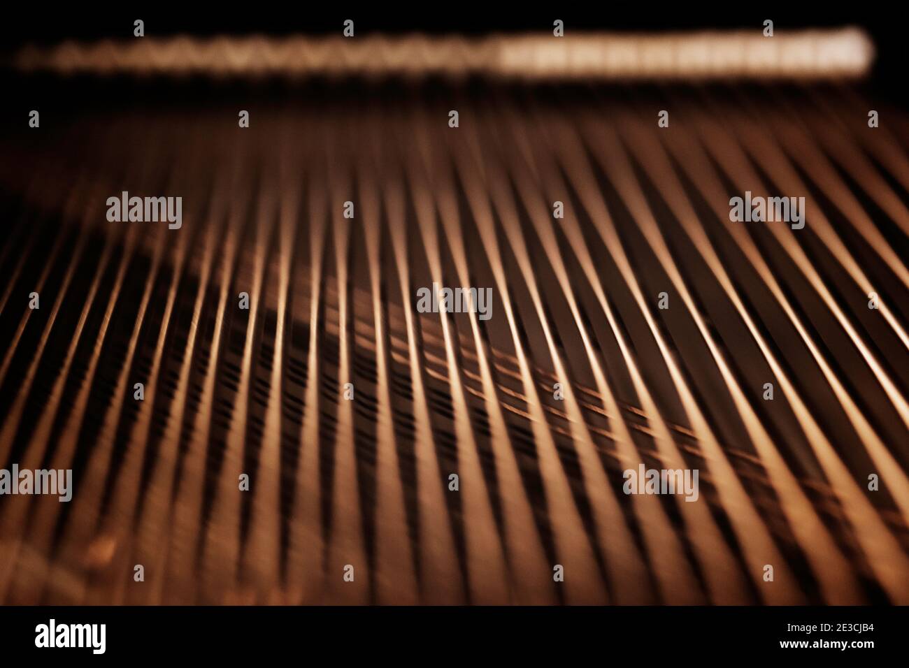 Die Streicher auf dem Resonanzboden eines Steinway M-Klaviers. Aufgenommen mit Licht aus den Glühbirnen im Zimmer. Stockfoto