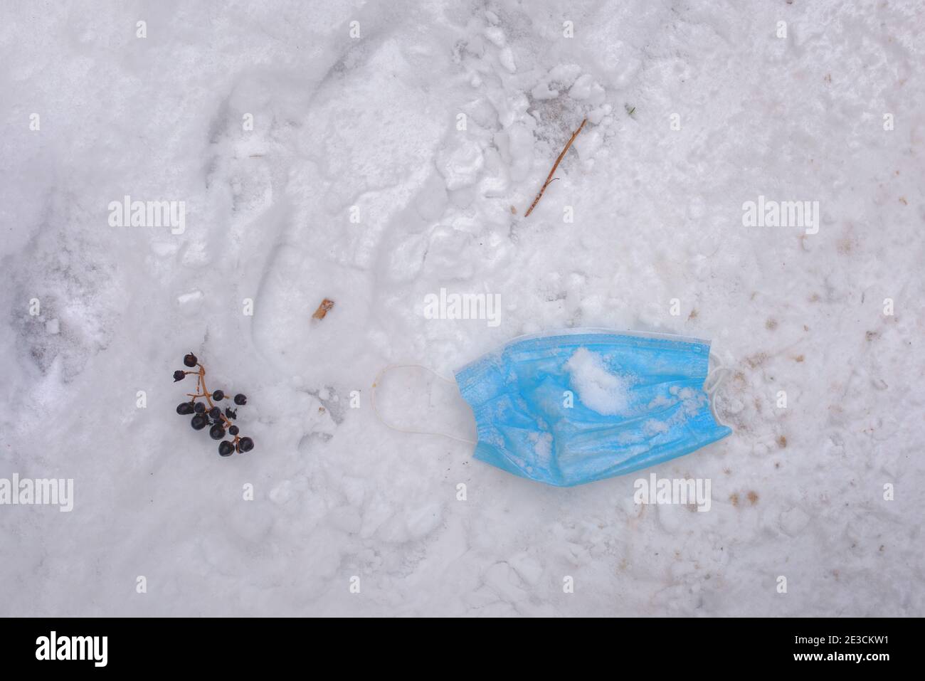 Gebrauchte medizinische Gesichtsmaske liegt auf verschneiten Boden. Öffentliche Räume werden mit ausrangierten Schutzausrüstungen überflutet. Stockfoto