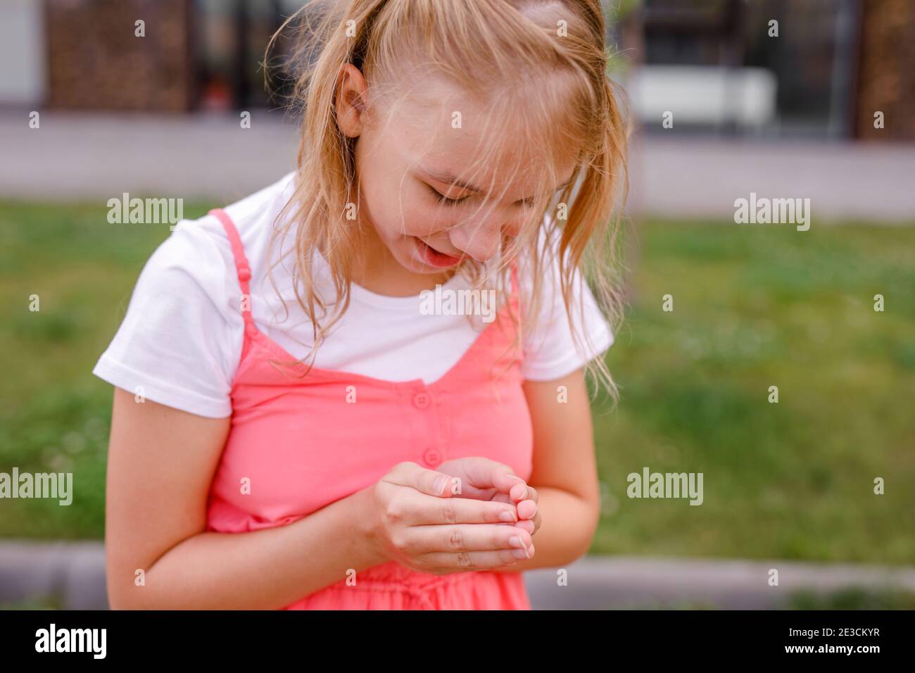 Ein Mädchen im Teenageralter in einer rosa Tunika fängt Insekten auf dem Gras vor ihrem Haus. Stockfoto