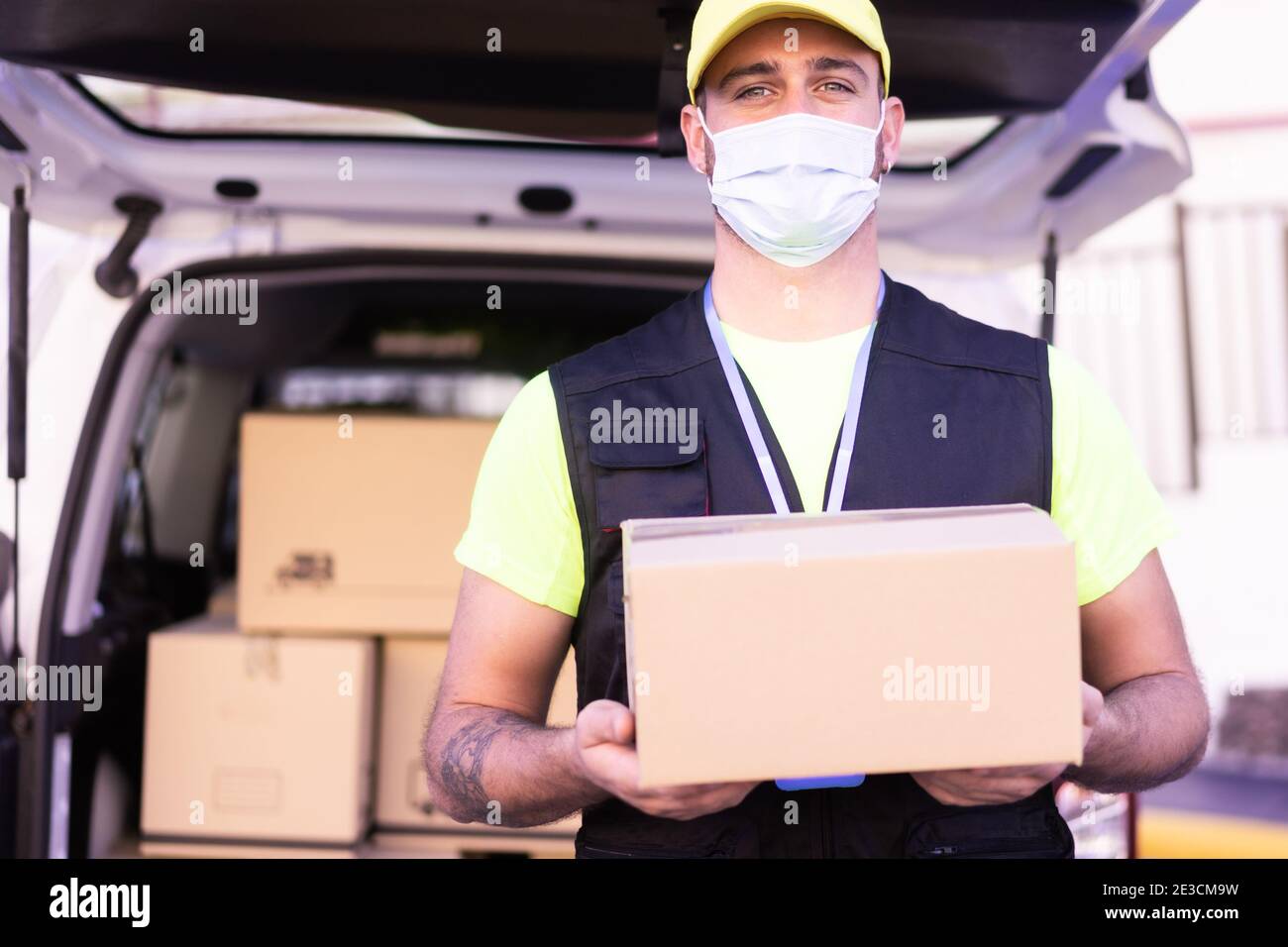 Liefermann Mitarbeiter in gelber Kappe und T-Shirt einheitliche Gesichtsmaske halten leere Karton-Box. Coronavirus und Kaufkonzept. Stockfoto