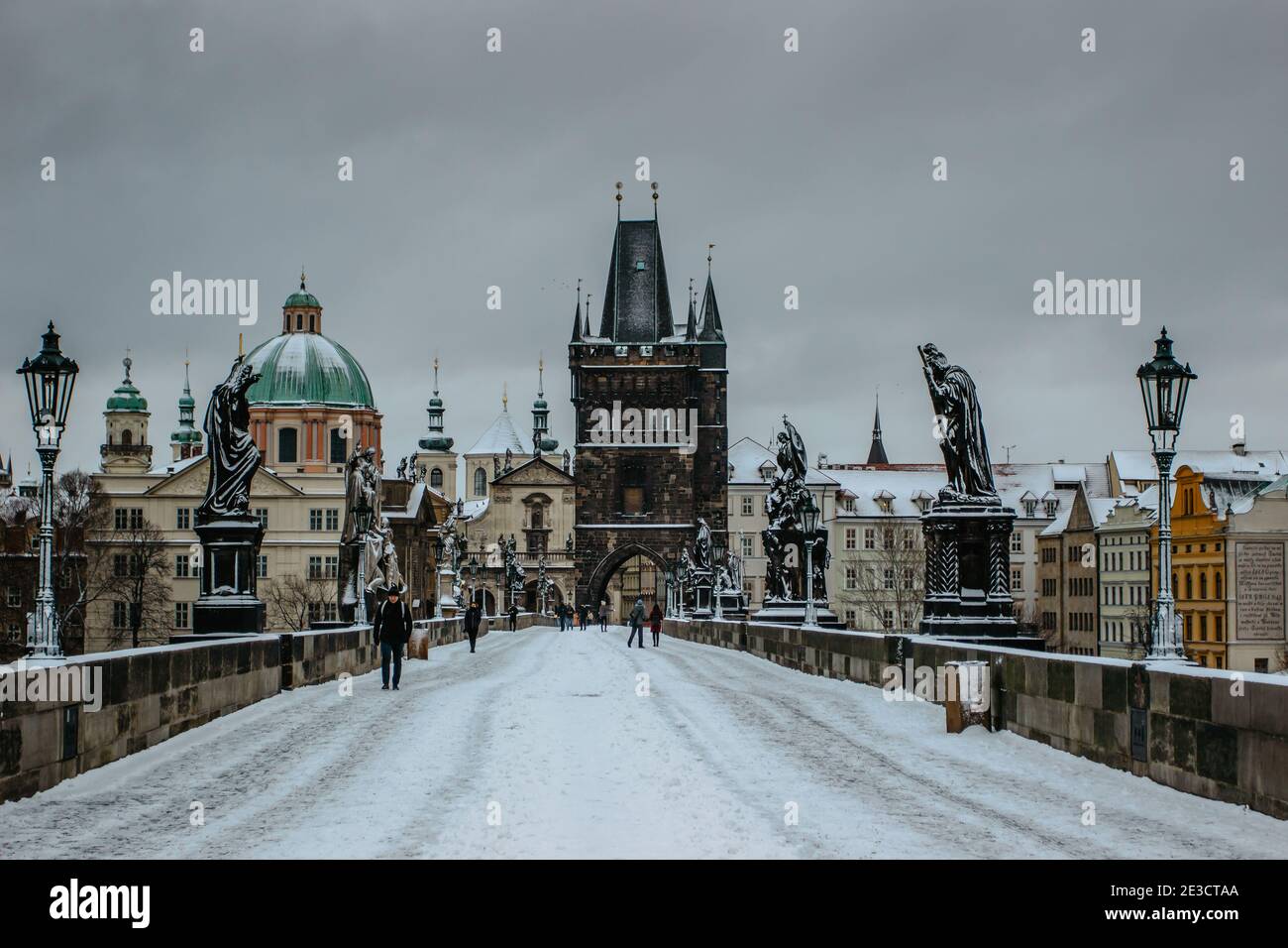 Prag, Tschechische Republik - 14. Januar 2021. Karlsbrücke, Altstädter Brückenturm mit Schnee bedeckt. Menschen, die im kalten Winter durch die Stadt wandern Stockfoto
