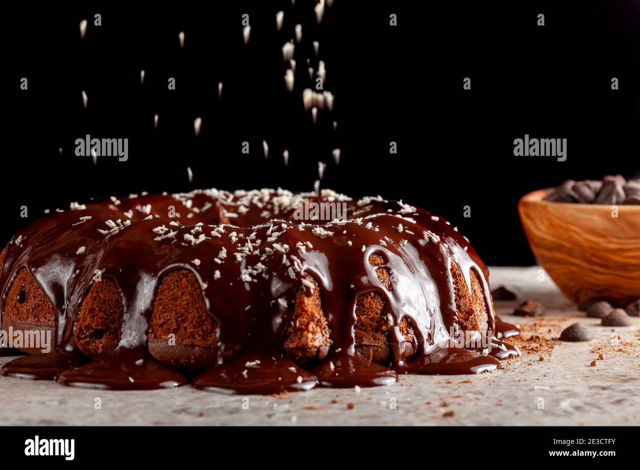 Seitenansicht eines frisch gebackenen Schokoladenkuchens auf weißer Steinplatte mit dunklem Hintergrund; geschmolzener Schokoladenpudding tropft an den Seiten mit Kokon Stockfoto