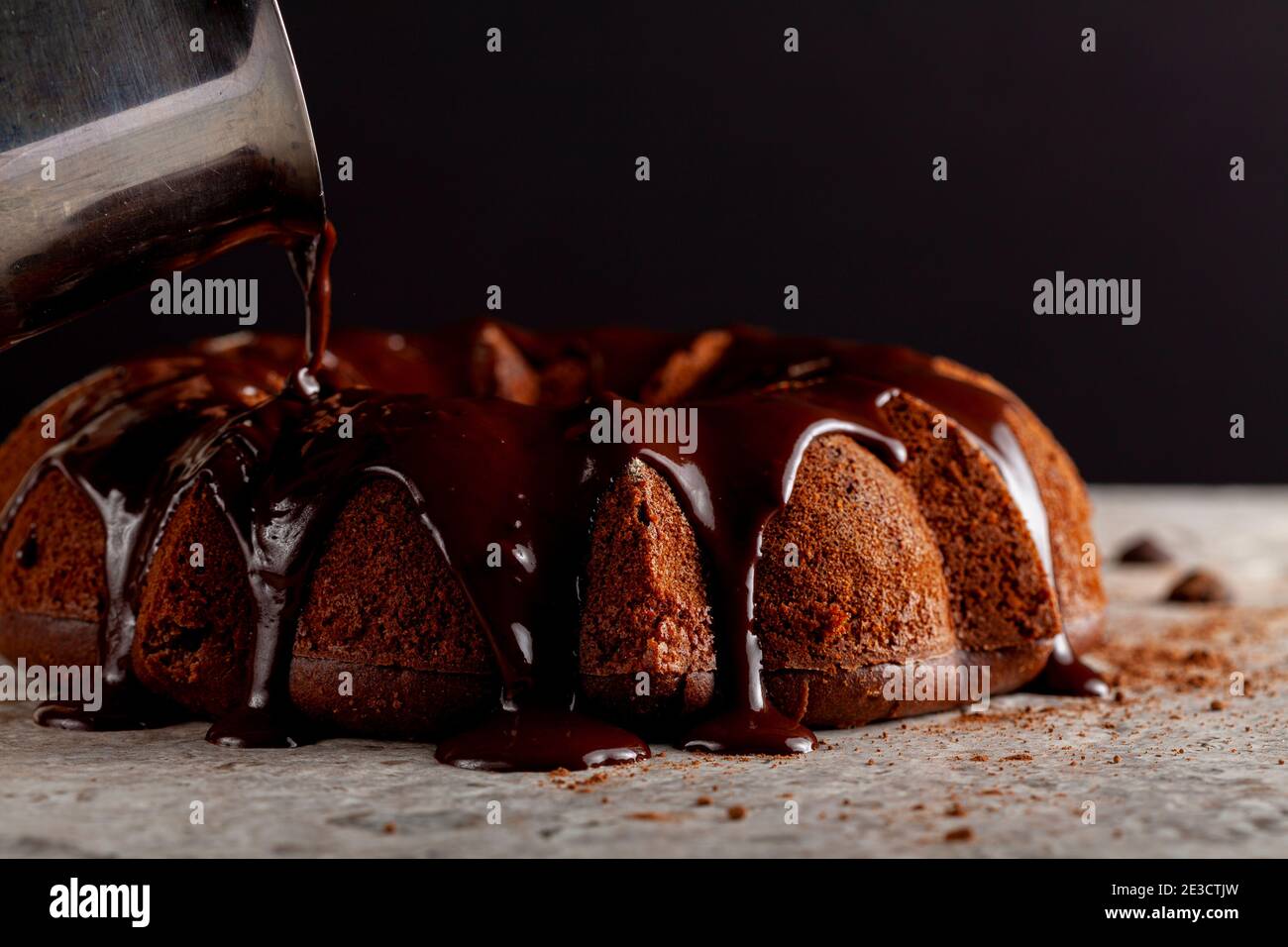 Geschmolzener heißer Schokoladenpudding wird von einem metallenen Kaffeekanne auf einen Schokoladenkuchen als Sahnehäubchen gegossen. Es fließt nach unten und macht braune Pfütze Stockfoto