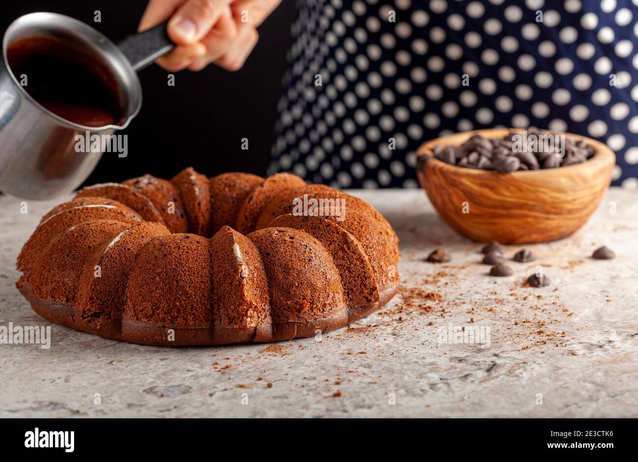 Ein Koch ist dabei, geschmolzene Schokolade auf einen runden Kuchen frisch aus dem Ofen zu gießen. Sie hält einen Krug aus Metall, in dem sich die geschmolzene Vereisung befindet. Der Stockfoto