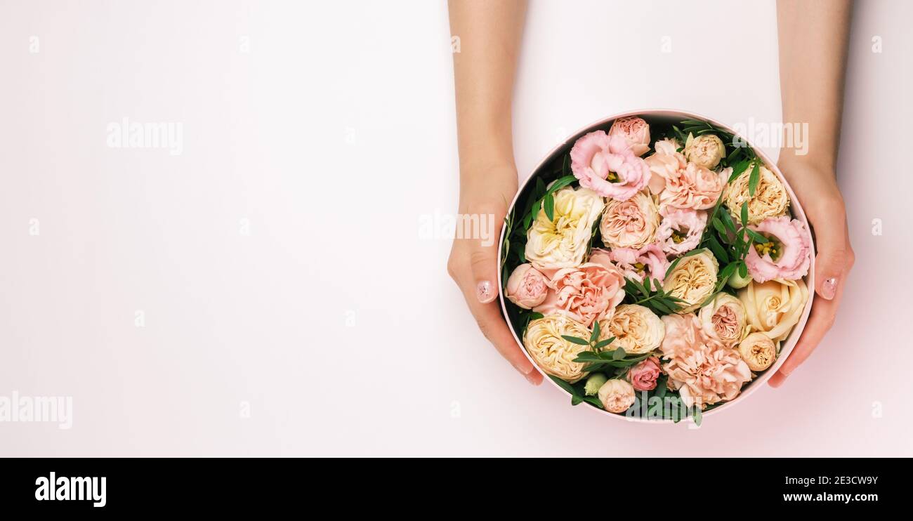 Florist hält einen Hut runde Box mit floralen Komposition auf einem rosa Hintergrund mit Copy Space. Geschenkbox für 8. März, Valentinstag, Muttertag Stockfoto
