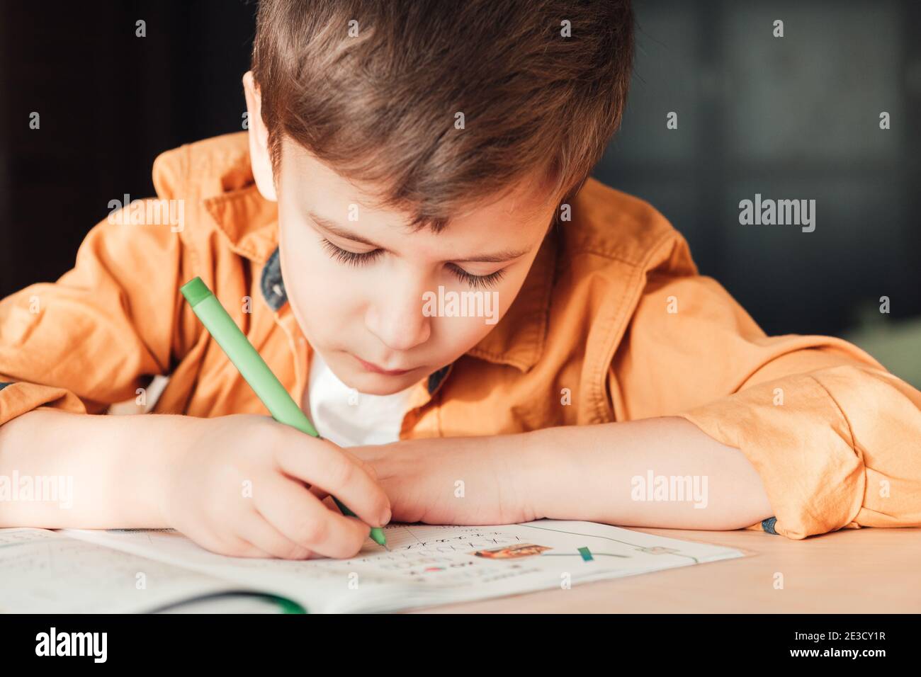 Nettes 7 Jahre altes Kind, das seine Hausaufgaben macht, am Schreibtisch sitzend. Junge schreiben in Notebook. Stockfoto