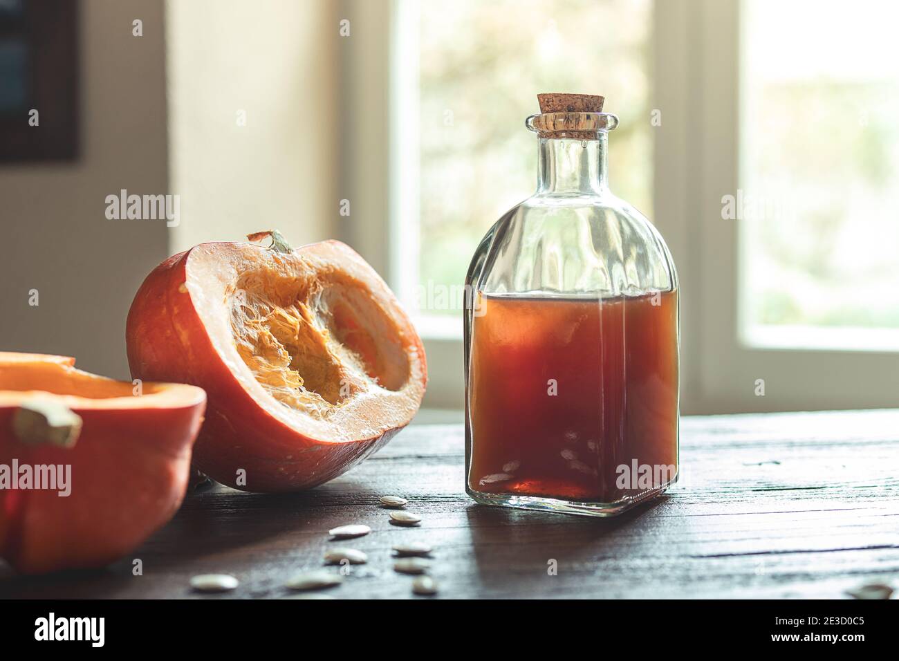 Eine Flasche Bio Kürbiskernöl und Stücke Frischer Kürbis auf einem Holztisch gegen ein Fenster Stockfoto