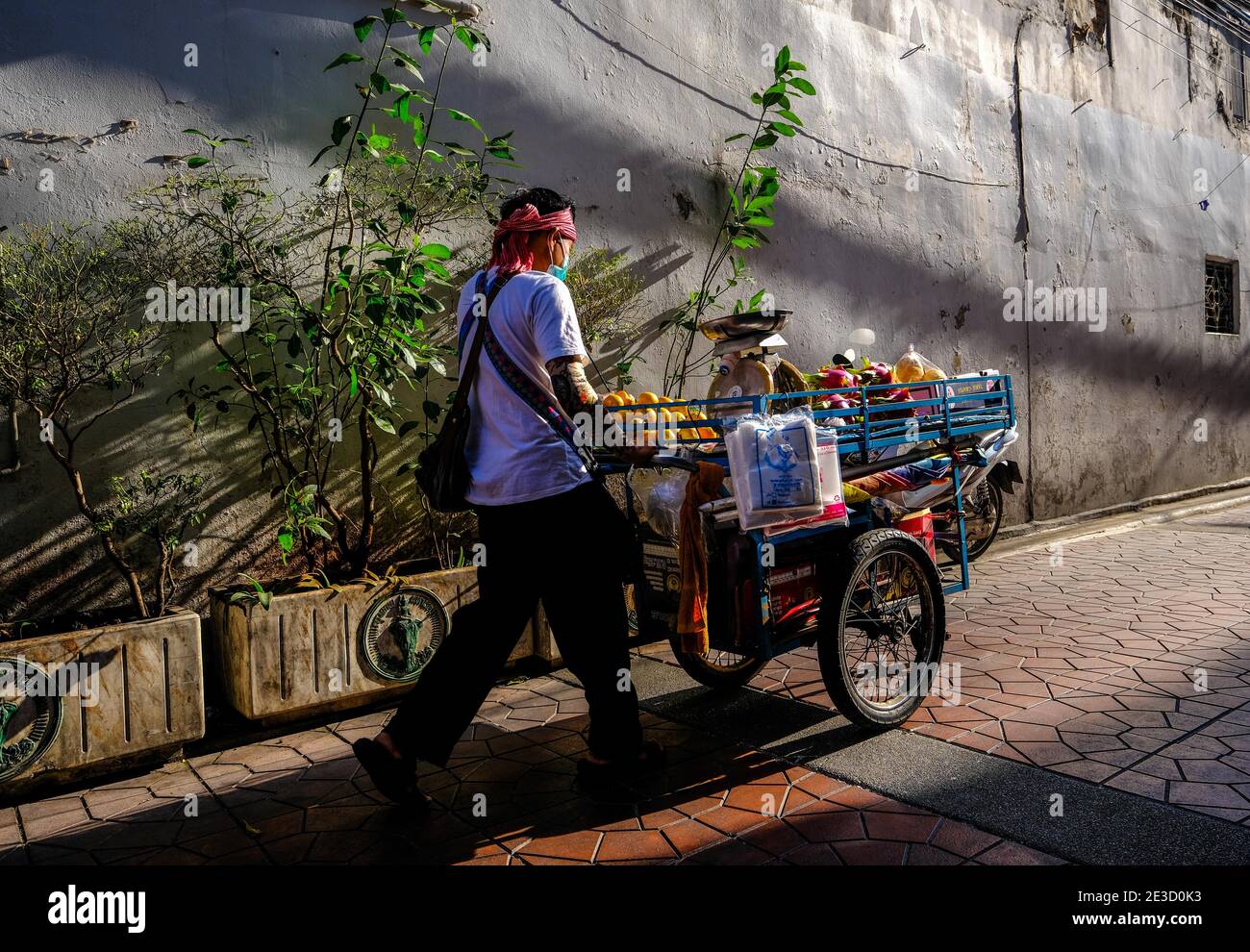 Ein männlicher Straßenverkäufer schiebt seinen Obstwagen entlang einer sonnenbeschienenen Straße in Chinatown, Bangkok, Thailand Stockfoto