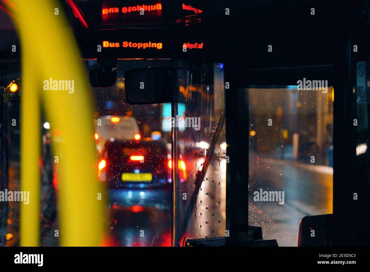 Bushalteschild blinkt am regnerischen Abend in den öffentlichen Verkehrsmitteln, verschwommene Straßen und Lichter Hintergrund Stockfoto