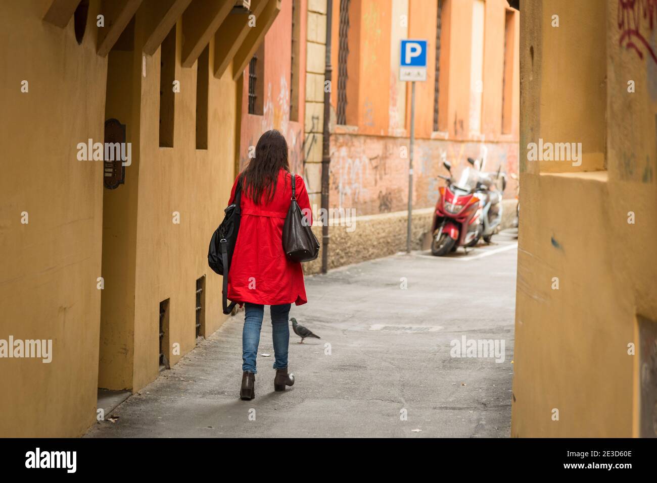 Eine Frau in einem roten Mantel geht eine schmale Straße in Bologna Italien Stockfoto