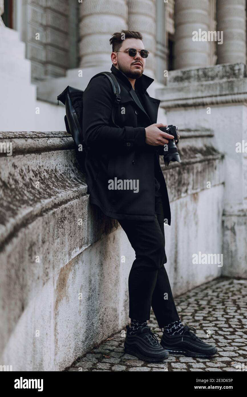 Voller Länge von jungen Kerl mit Kamera Aufenthalt in der Stadt mit Gebäude im Hintergrund. Reisekonzept Stockfoto