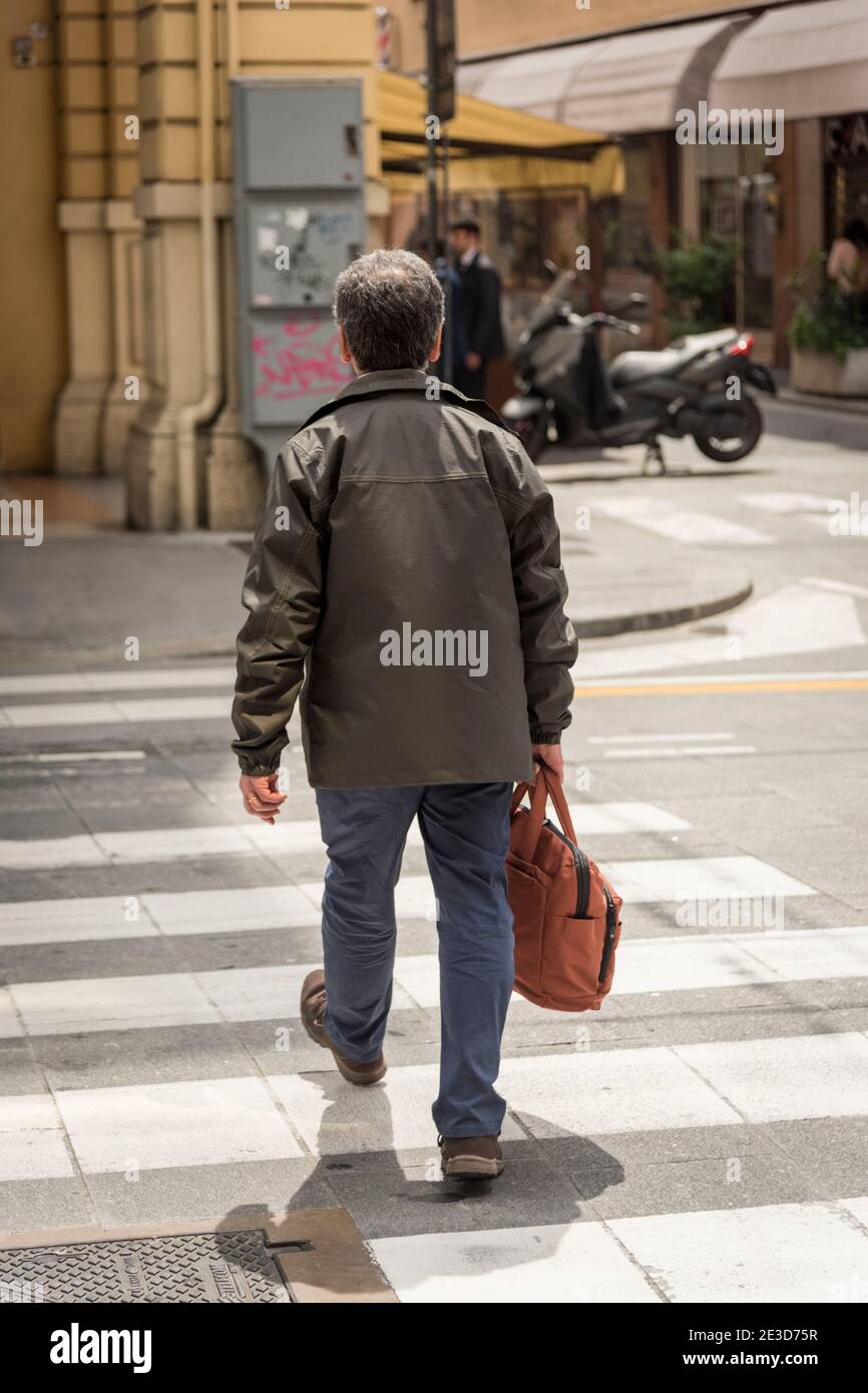Ein Mann mittleren Alters in einem Ledermantel Fußgängerüberweg Bei Sonnenschein in Bologna italien Stockfoto