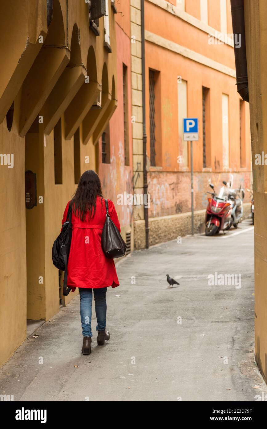 Eine Frau in einem roten Mantel geht eine schmale Straße in Bologna Italien Stockfoto