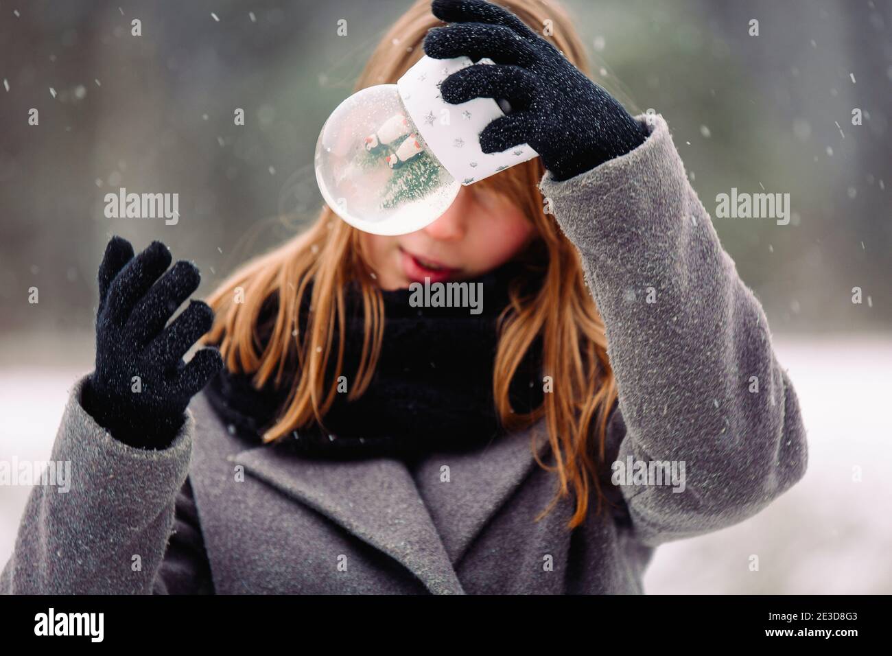 Ein hübsches Mädchen in Überraschung schüttelt eine Glas Winter Schneekugel vor ihrem Gesicht. Vergrößertes Foto von magischen Seite im Winter magischen Hintergrund mit Stockfoto