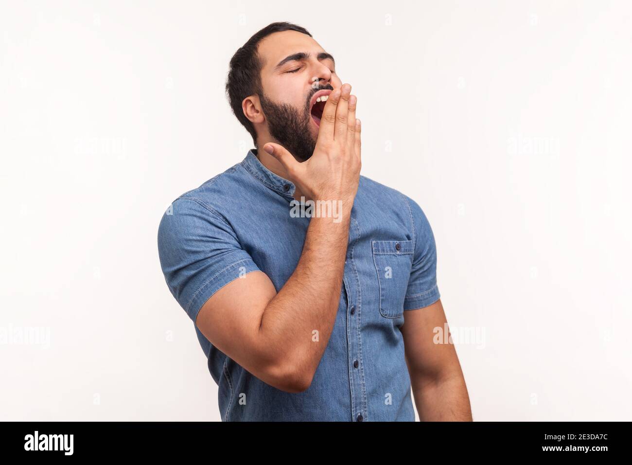 Müde schläfriger Mann mit Bart gähnend, Mund schließen mit der Hand, Mangel an Energie, Schlaflosigkeit in der Nacht und frühen Erwachen, Überarbeiten. Studio im Innenbereich Stockfoto
