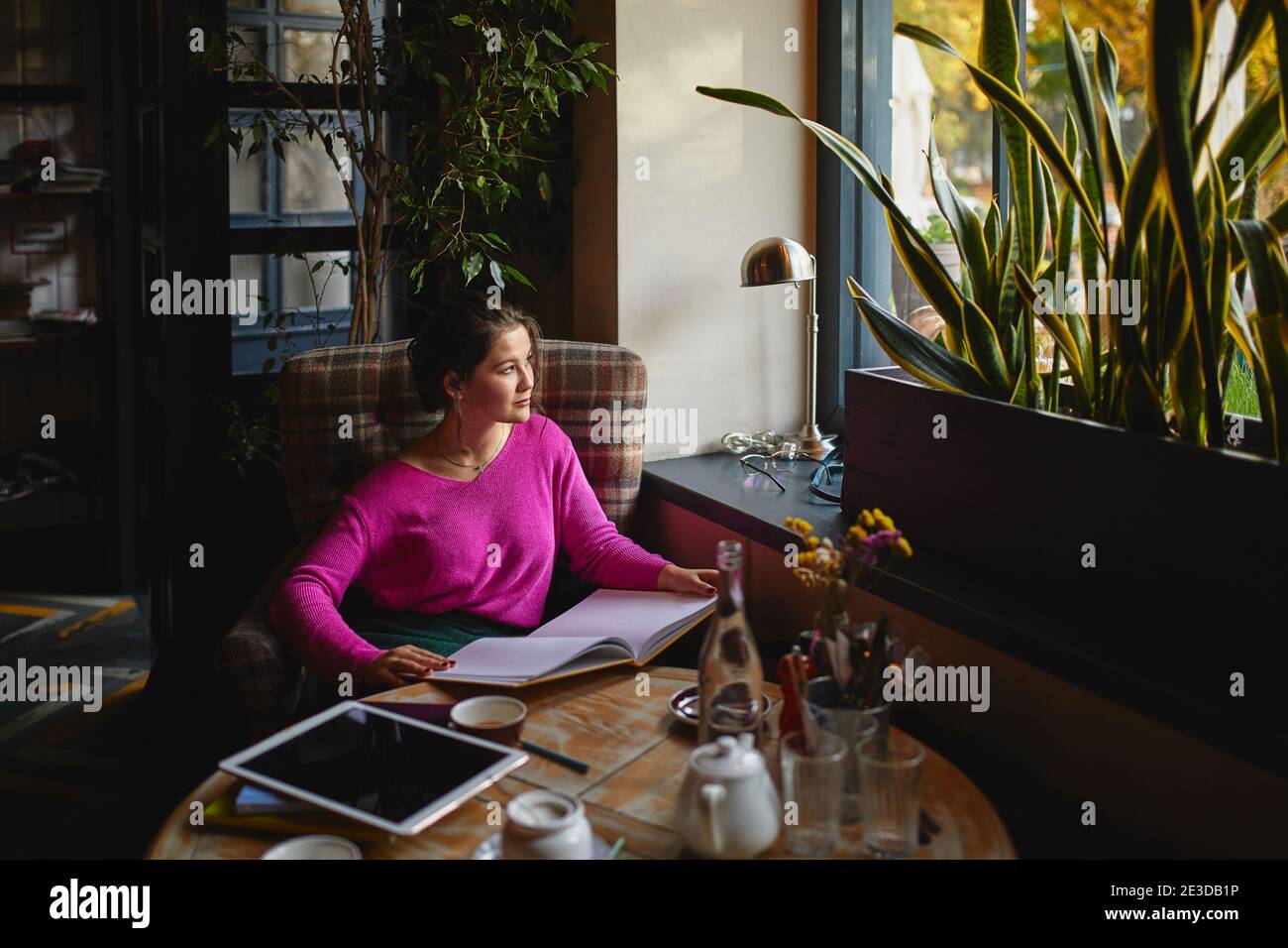 Attraktive lächelnde Frau hält Menü, während sie sich in einem gemütlichen Café ausruhen Stockfoto