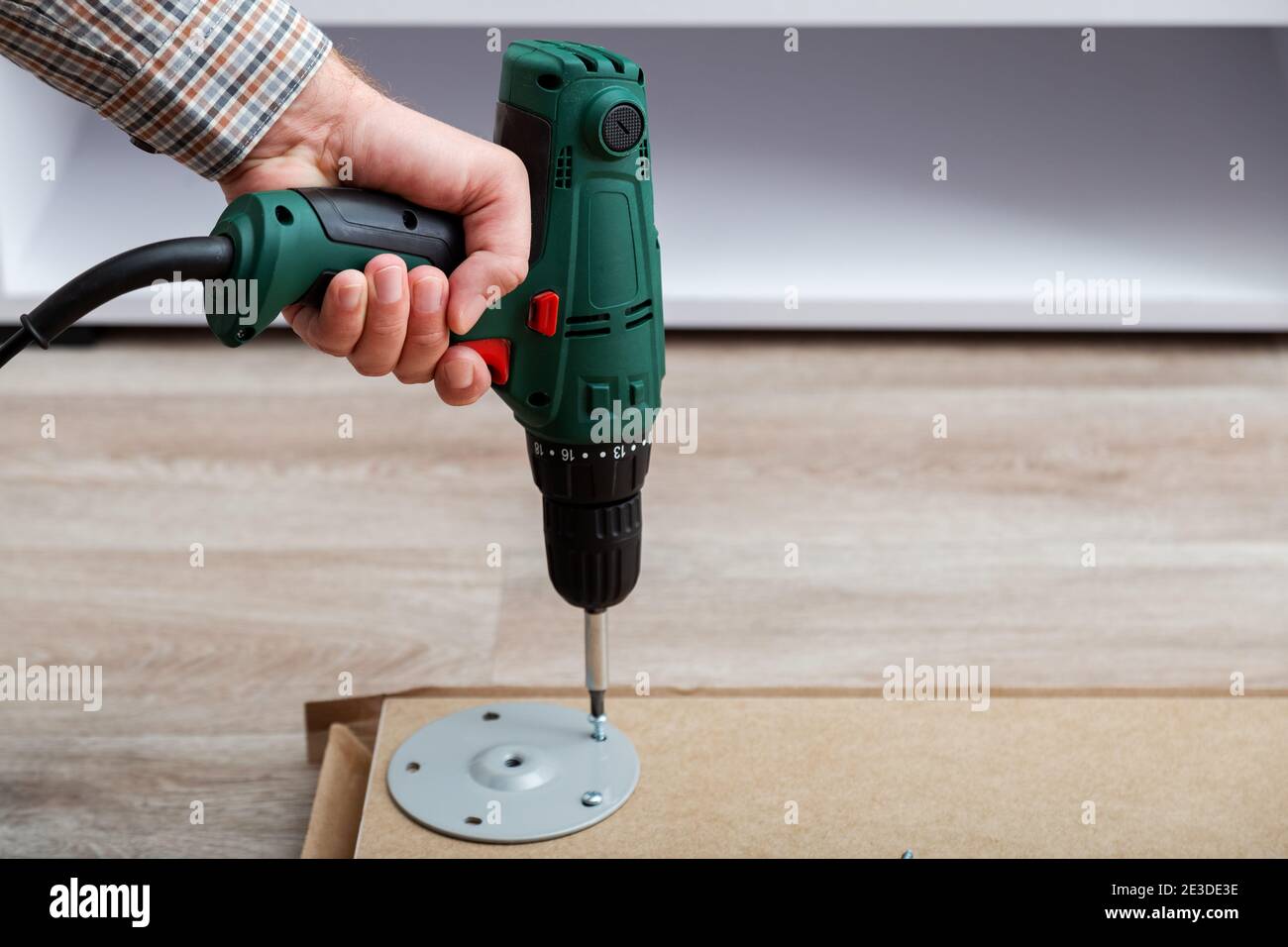 Mann montiert Tischmöbel mit Bohrer. Montage, Möbelreparatur Hausmeister. Männliche Hand mit Bohrer auf dem Boden. Speicherplatz kopieren Stockfoto
