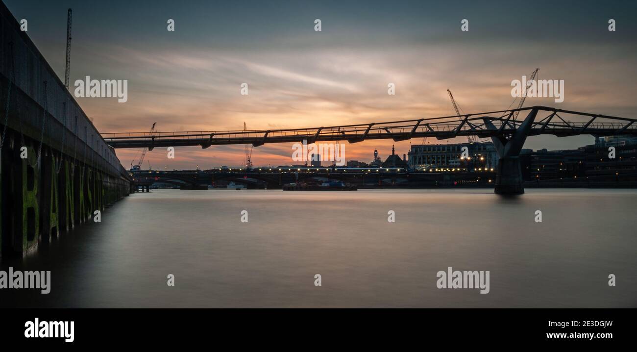 Die Sonne geht über der Themse, der Millennium Bridge und der Londoner Skyline unter, von der Londoner Bankside aus gesehen. Stockfoto