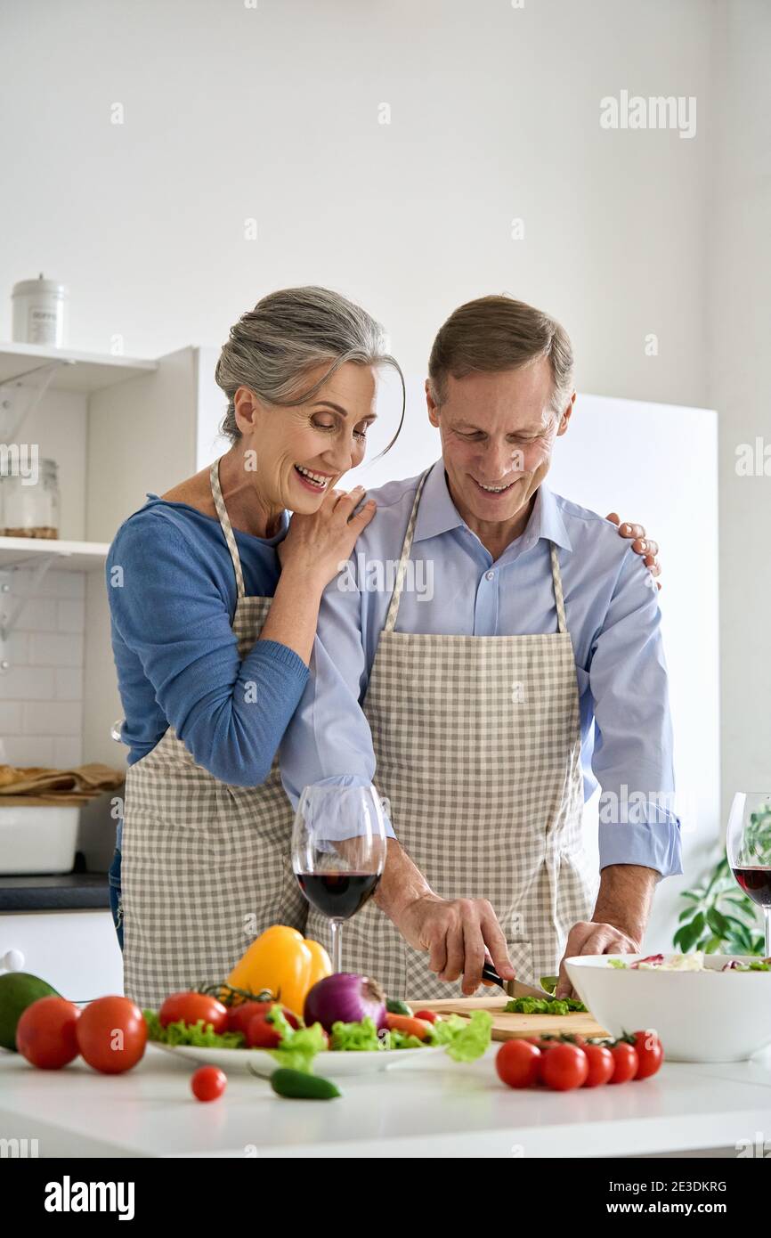 Glückliches älteres veganes Paar, das gesunden Gemüsesalat zu Hause in der Küche zubereitet. Stockfoto