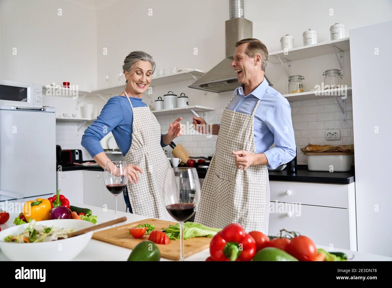 Glückliches Seniorenpaar, das zu Hause gemeinsam tanzt und gesundes Essen kocht. Stockfoto