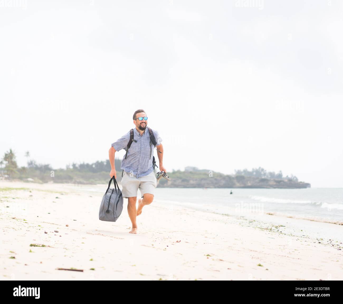 Fröhlicher erwachsener Mann mit Tasche Spaß auf der tropischen Strand Stockfoto