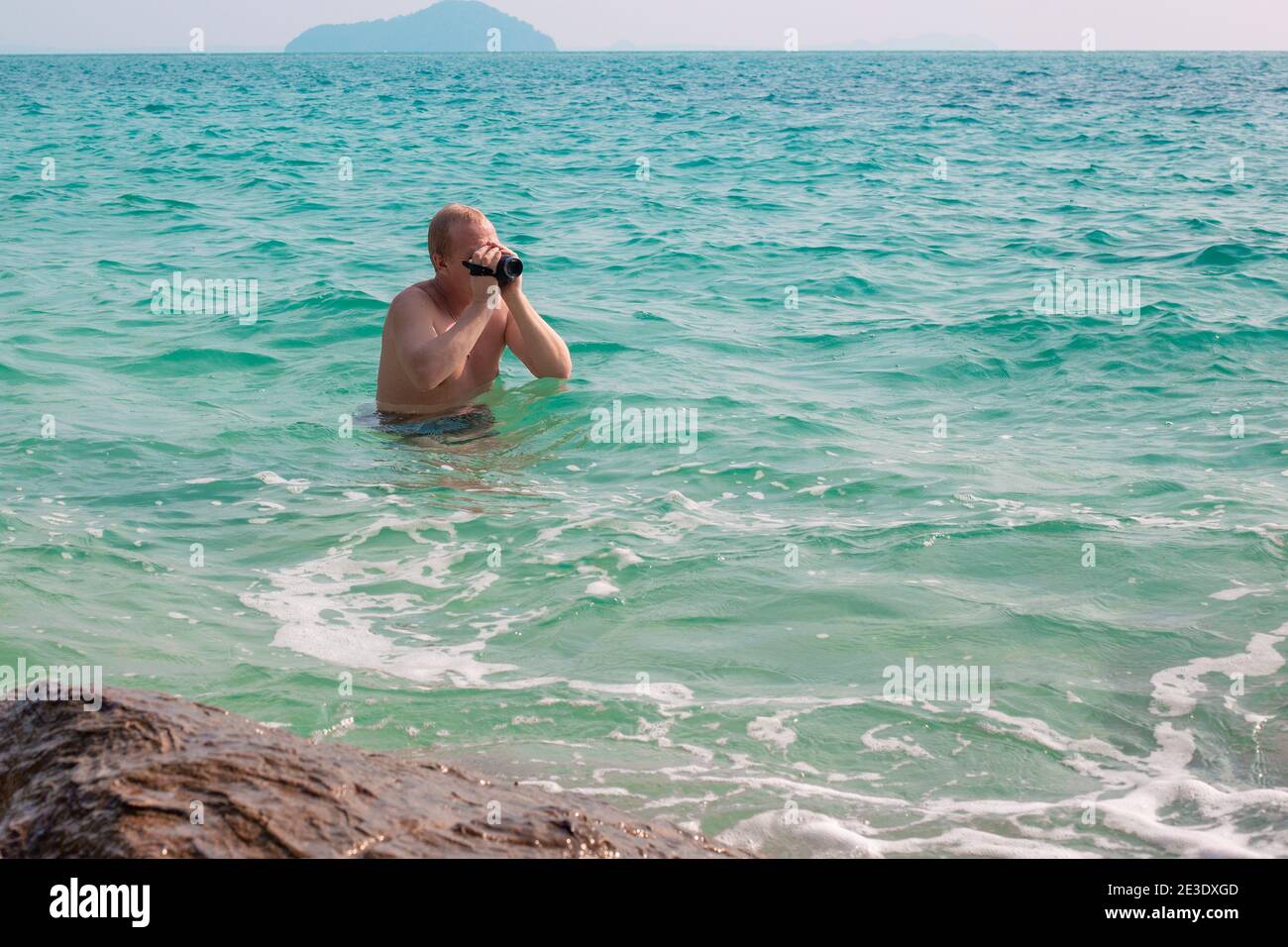 Ein Europäer steht tief im Wasser und fotografiert Seebilder auf einer Videokamera, ein Blogger bereitet Materialien, Reisen und Tourismus vor Stockfoto